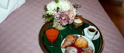 Una bandeja de desayuno con pasteles, un vaso de jugo de naranja y una taza de café sobre una cama con colcha acolchada rosa.