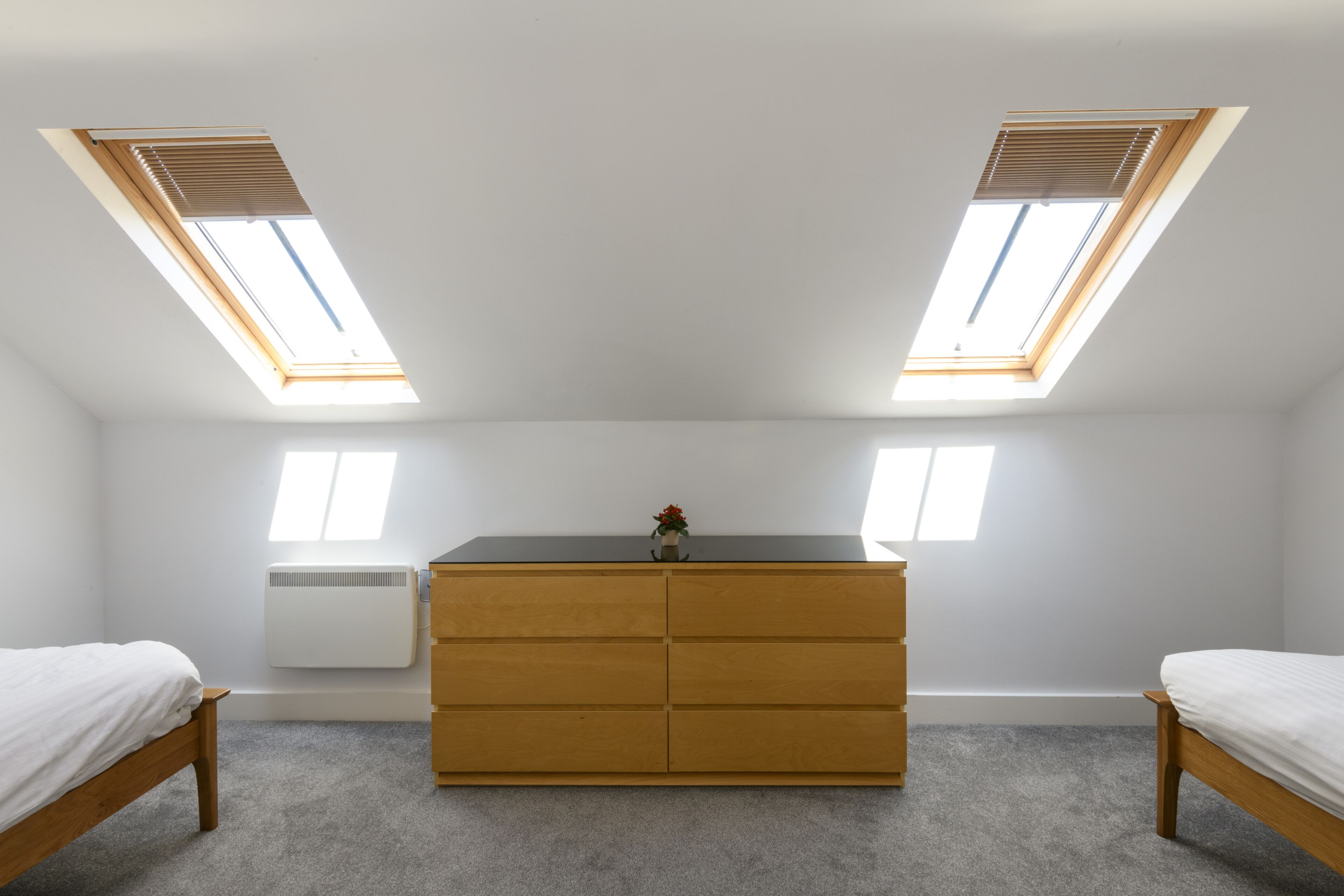 Un dormitorio con cómoda de madera, dos camas y tragaluces.