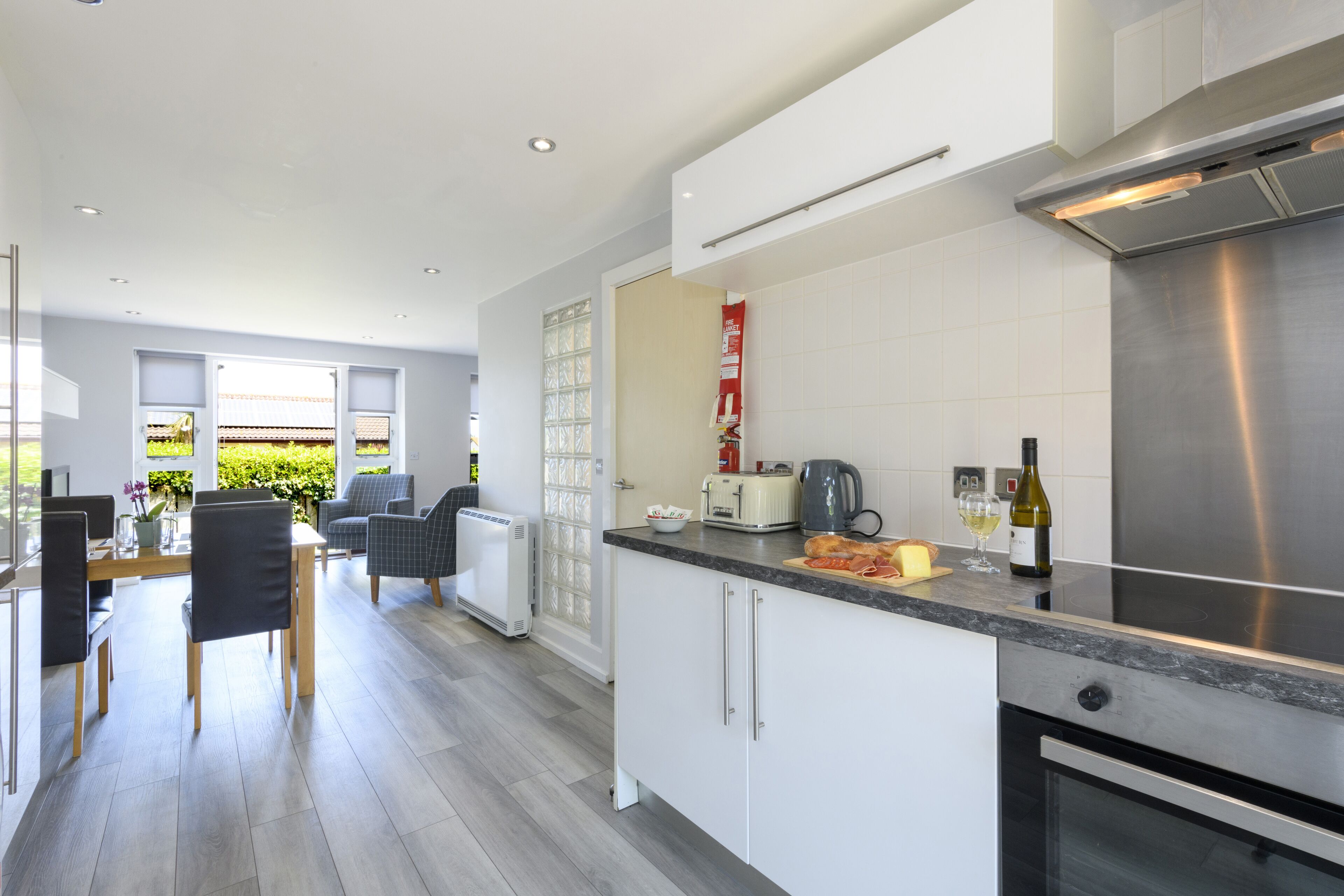 A modern kitchen with white cabinets, a stainless steel range hood, and a dining area with a table and chairs.