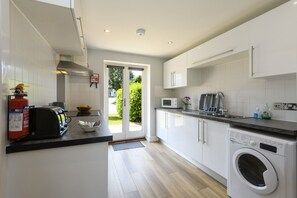 A modern kitchen with white cabinets, a built-in microwave, a toaster, and a washing machine. - Bay Retreat Villas (Padstow)
