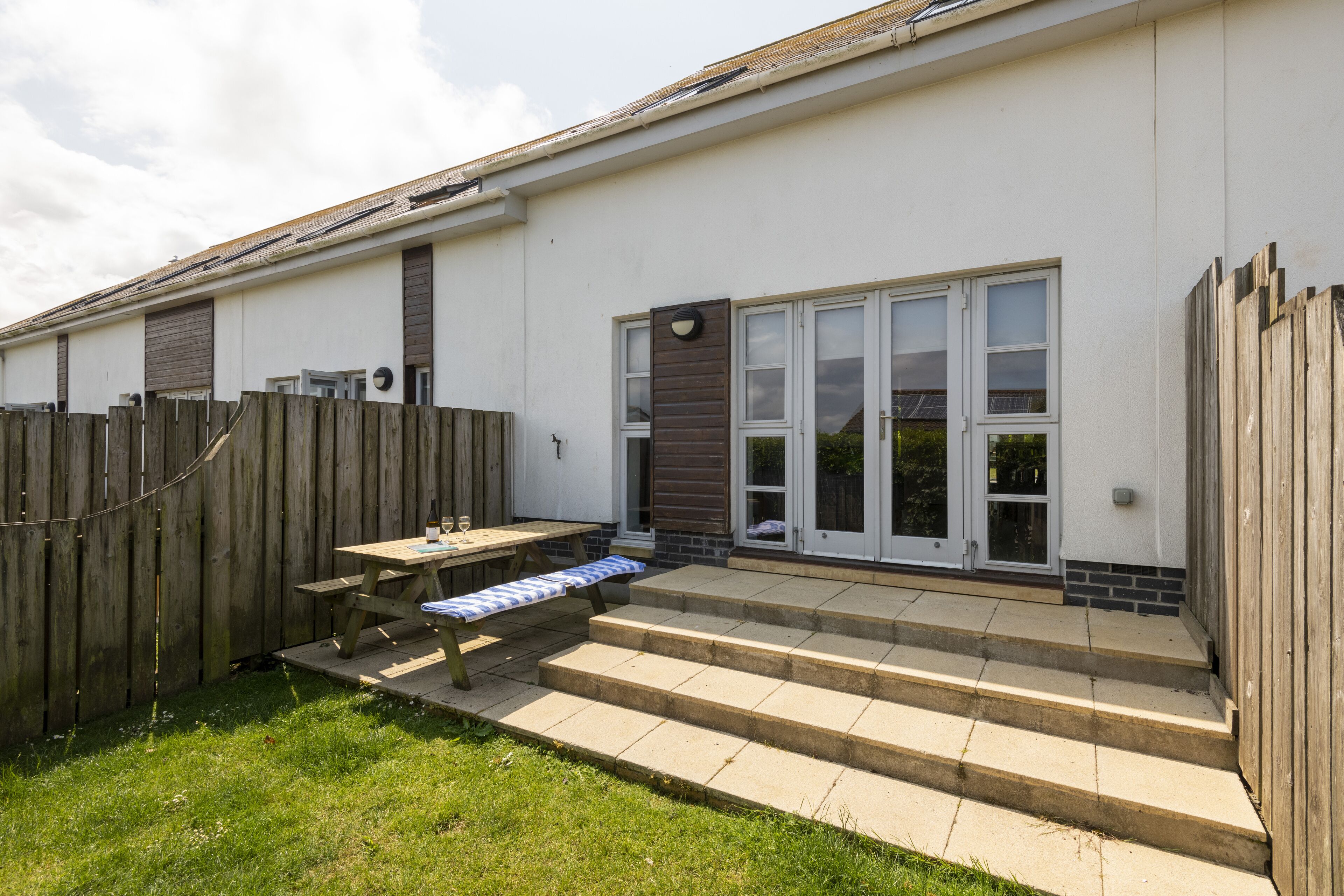 A residential building with a wooden deck, a picnic table, and a set of steps leading to a front door.
