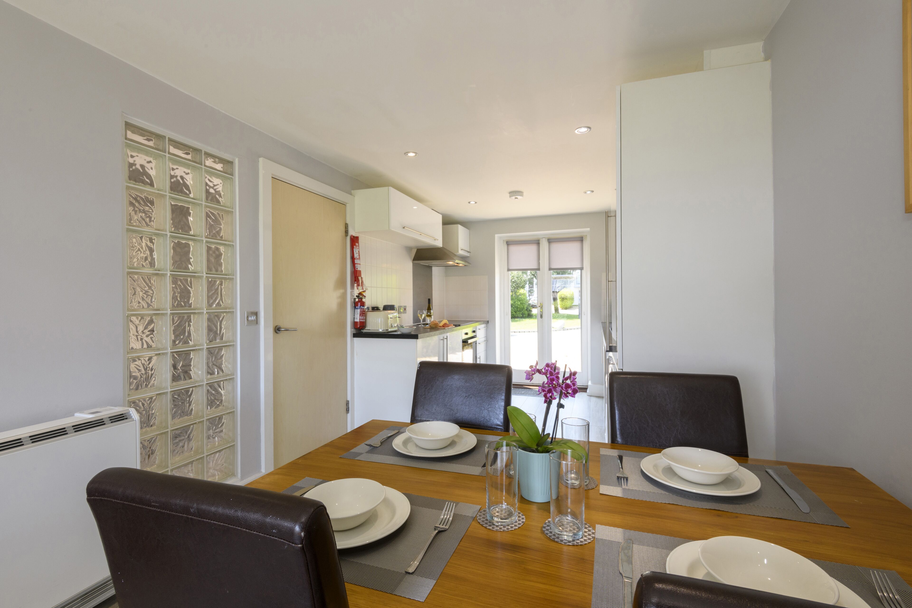 A dining area with a wooden table set for four, surrounded by chairs.