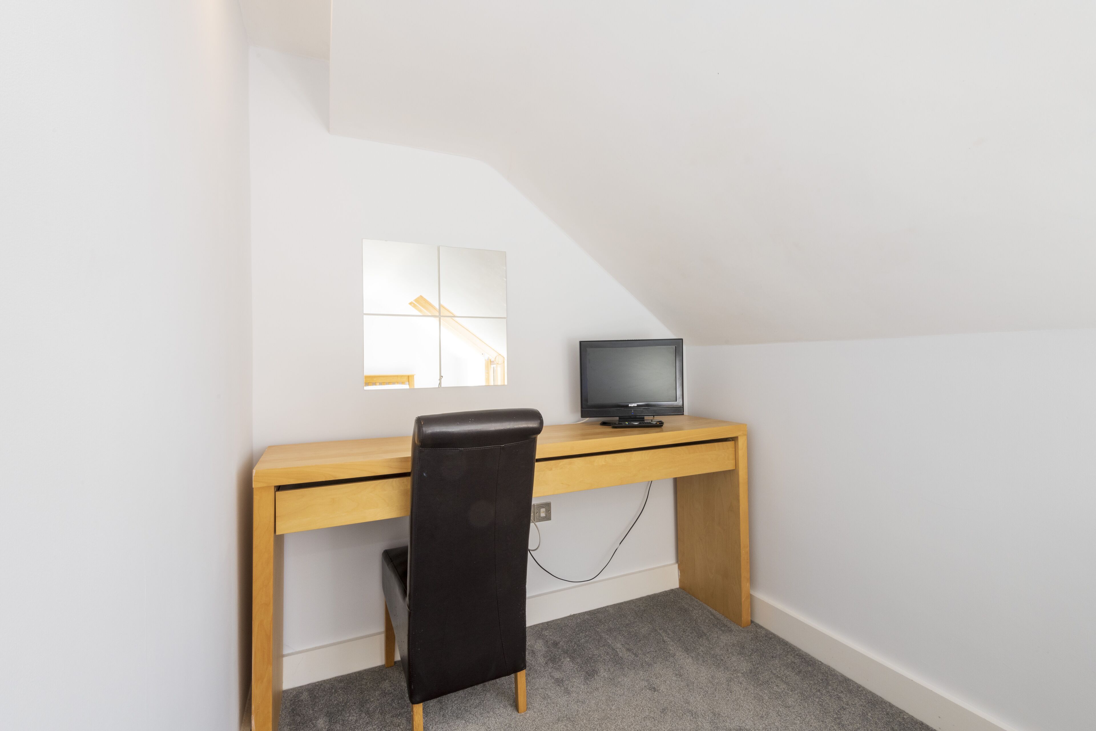 Una habitación pequeña y sencilla con un escritorio, una silla, un televisor y una ventana.