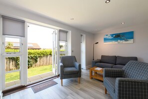 A living room with a sofa, armchairs, and a coffee table. There is a sliding glass door leading to a garden. - Bay Retreat Villas (Padstow)