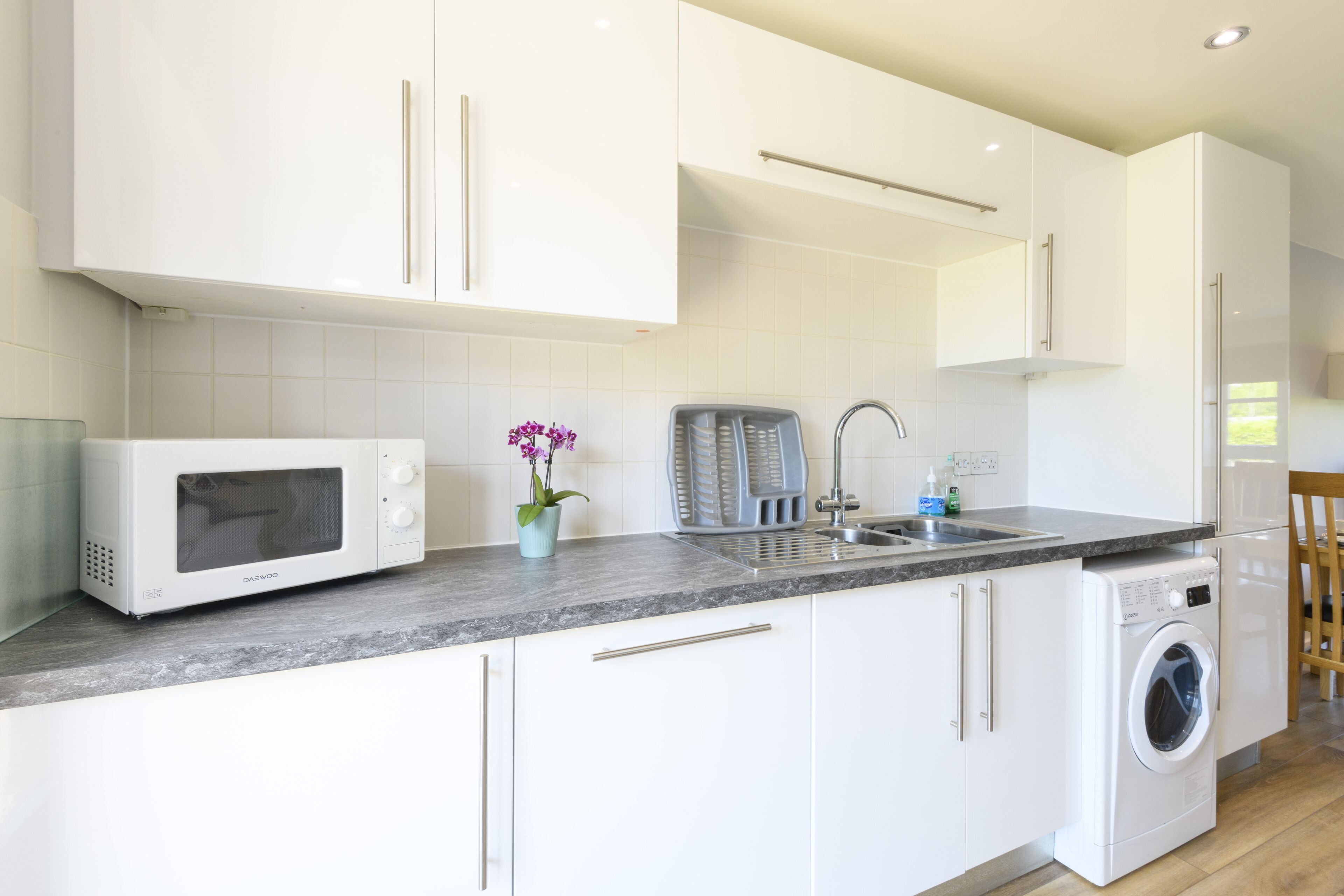 A modern kitchen with white cabinets, a microwave, a toaster, and a washing machine.