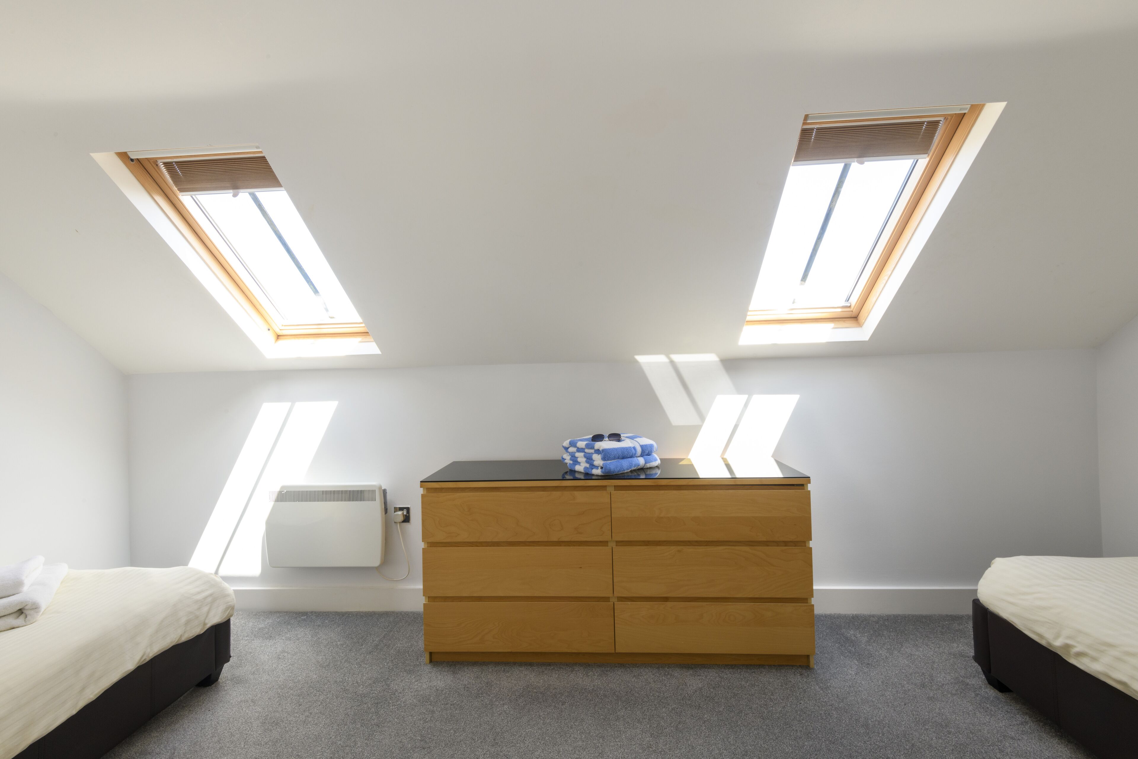 A bedroom with two skylights, a wooden dresser, and a bed.