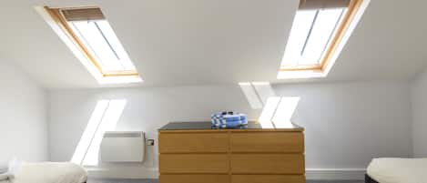 Een slaapkamer met twee dakramen, een houten dressoir en een bed.