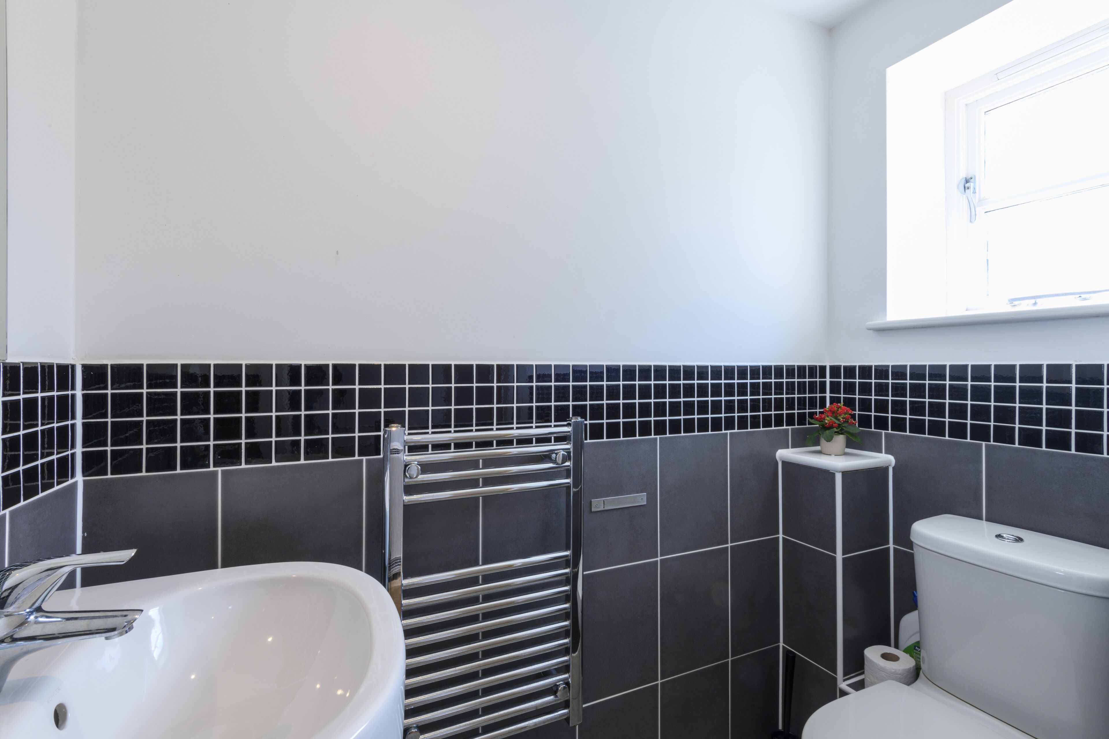 A bathroom with a white sink, a towel rack, a toilet, and a window with a view.
