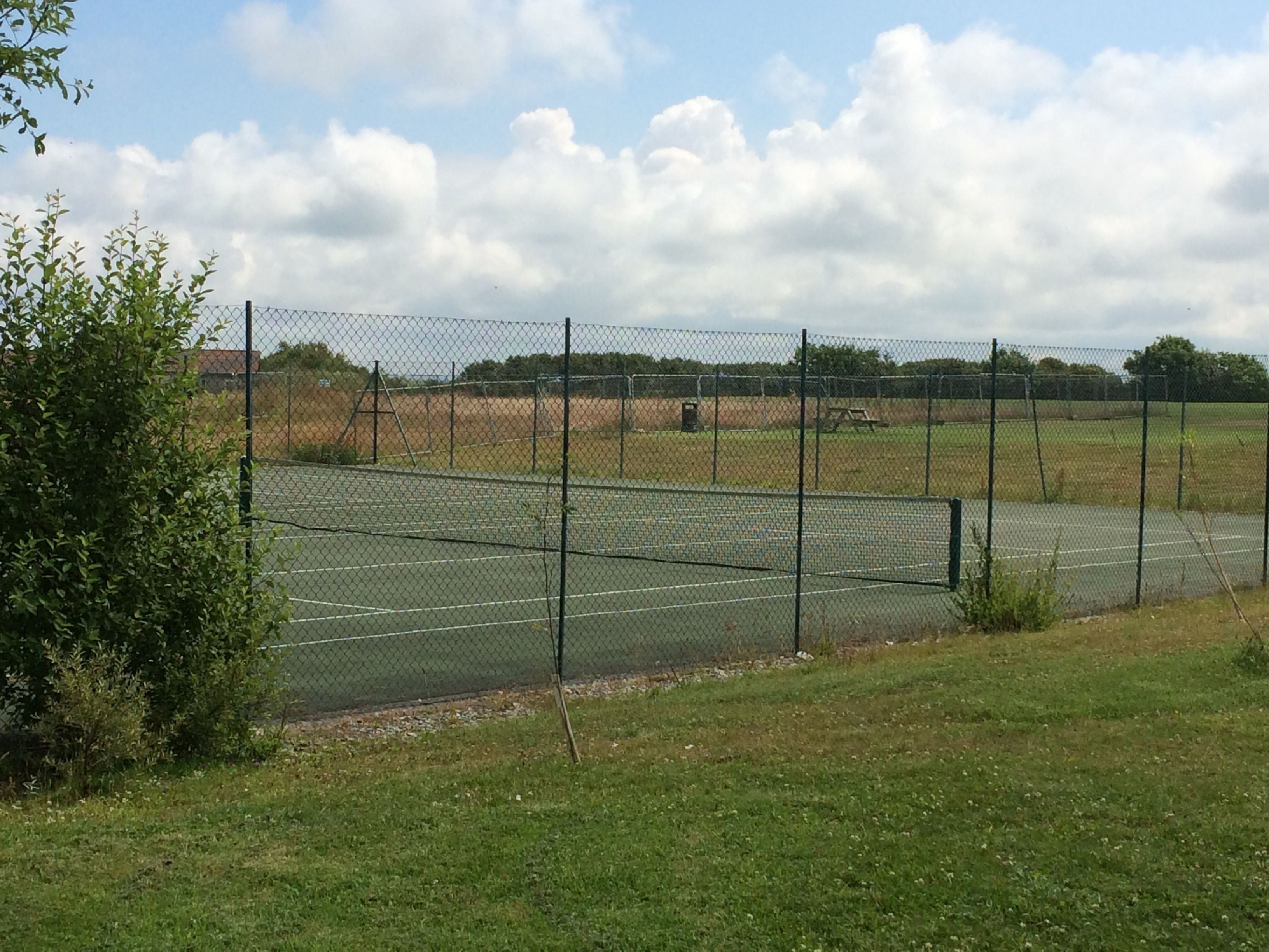 Un campo da tennis recintato con un prato sullo sfondo.