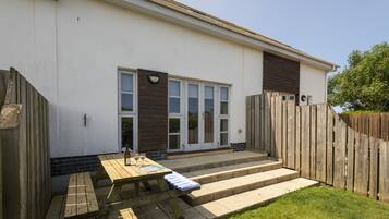 A patio with a wooden table and benches, a set of steps leading to a door, and a wooden fence surrounding the area.