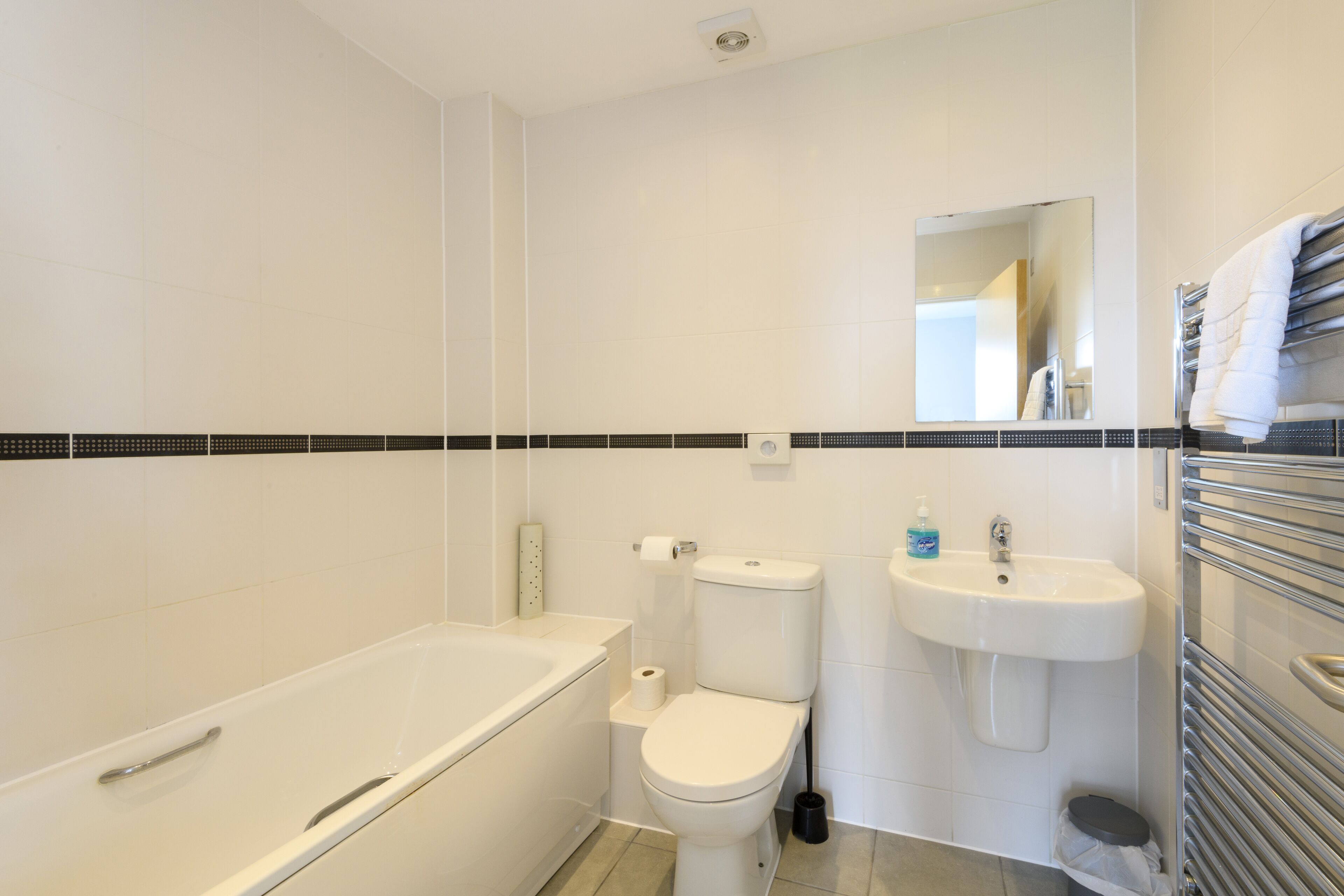 Et moderne badeværelse med badekar, toilet, vask og håndklædestang.