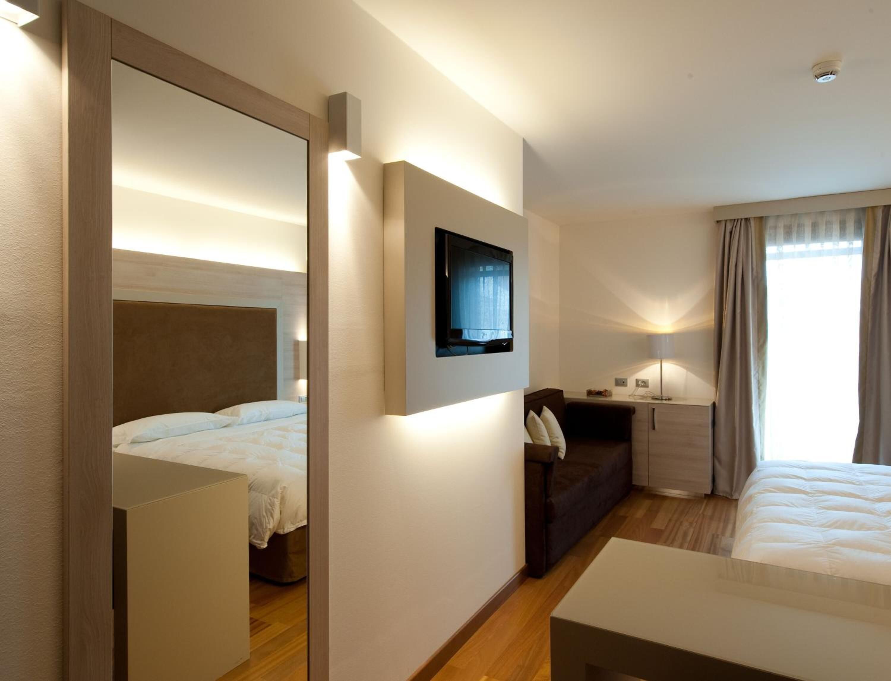 A hotel room with a bed, a sofa, a TV mounted on the wall, and a bedside table.