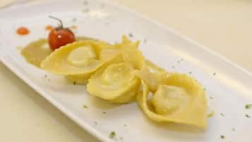 Ein Teller mit Ravioli und einer Kirschtomate.