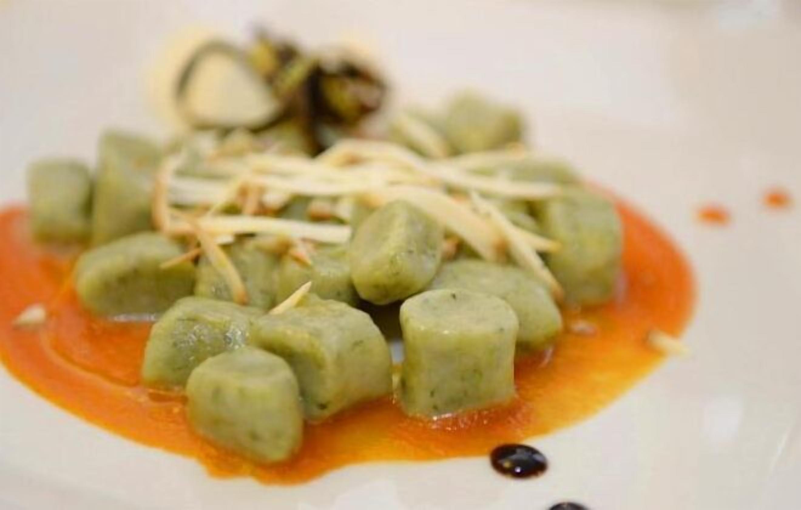 A dish with green dumplings, shredded cheese, and a red sauce on a white plate.