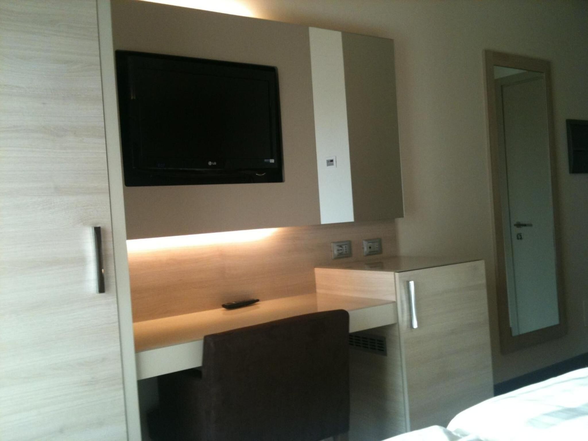 Habitación de hotel con cama, escritorio, silla, televisor sobre el escritorio y una puerta.