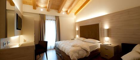 Un dormitorio con techo de madera, una cama con ropa blanca, una mesita de noche con lámpara y otro mueble auxiliar.