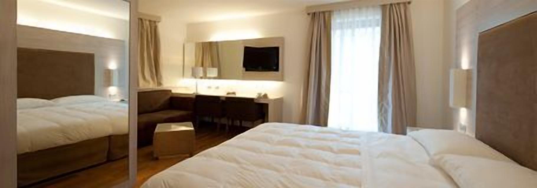 Habitación de hotel con una cama grande, un escritorio, una silla, un televisor y un espejo.