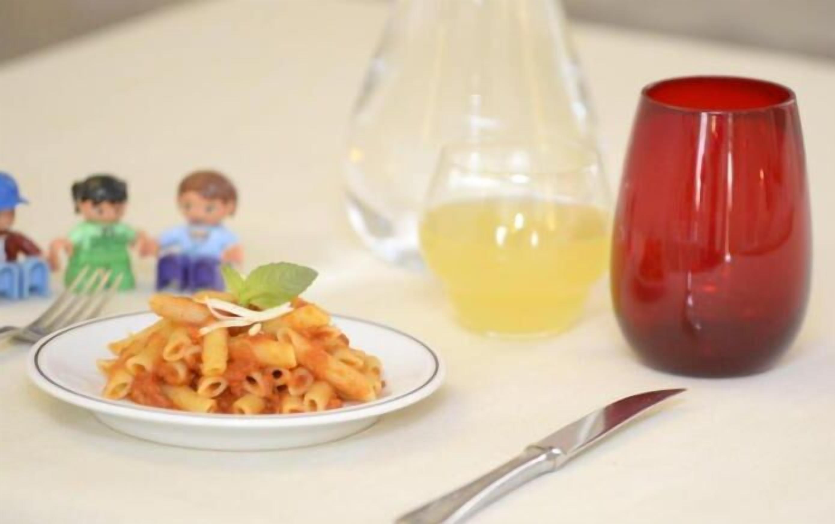 A plate of pasta with a small garnish, a glass pitcher, and a red cup on a table.