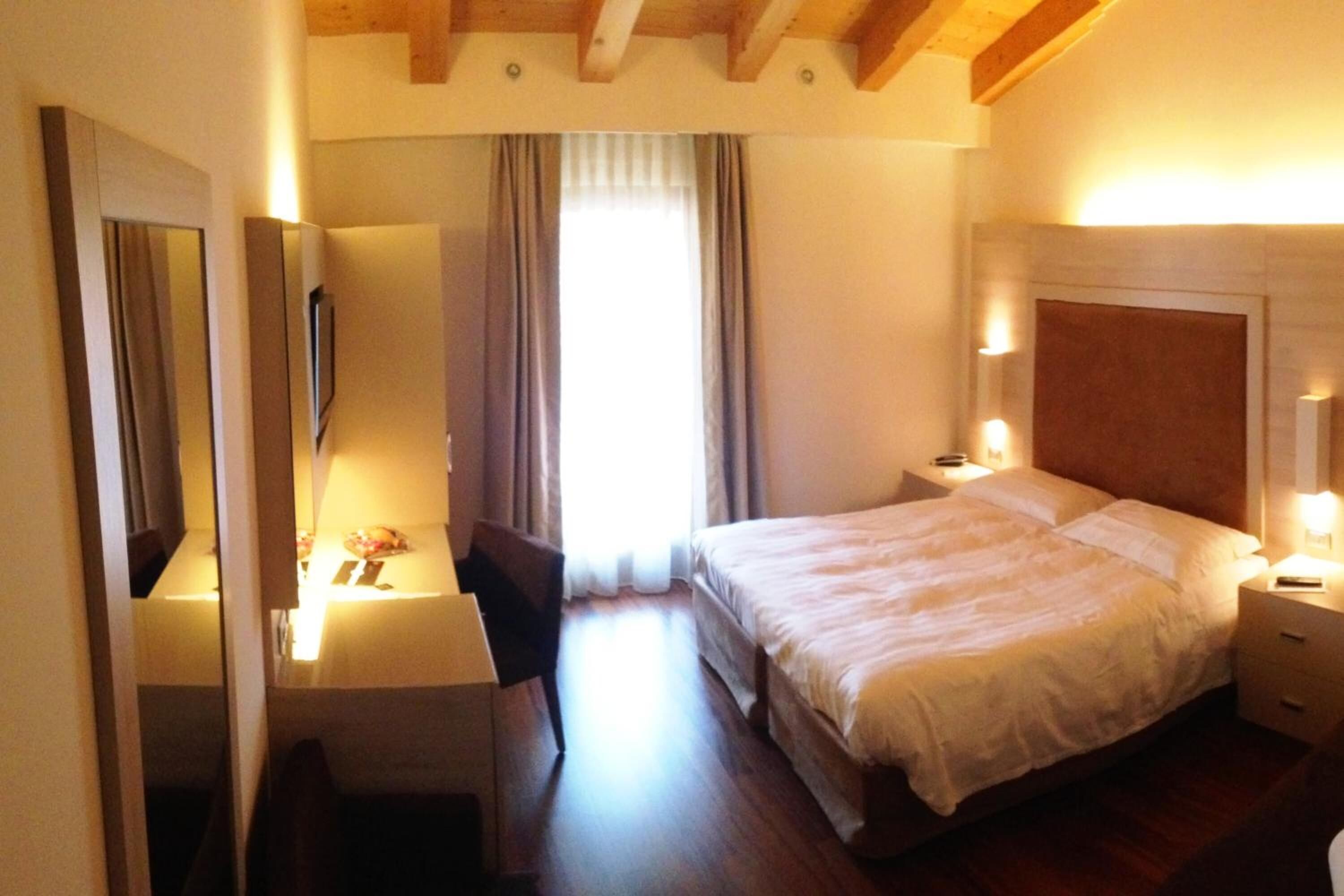 A hotel room with a bed, bedside table, lamp, and a desk with a chair.