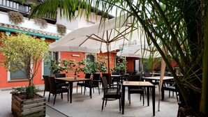 Un espace café en plein air, avec des tables et des chaises, entouré de plantes en pot et de parasols.