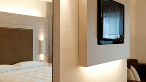 Une chambre d’hôtel moderne équipée d’un lit, d’un grand miroir et d’un téléviseur à écran plat fixé au mur.