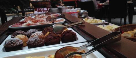 A buffet with various desserts and pastries, including brownies and macarons, with serving utensils.