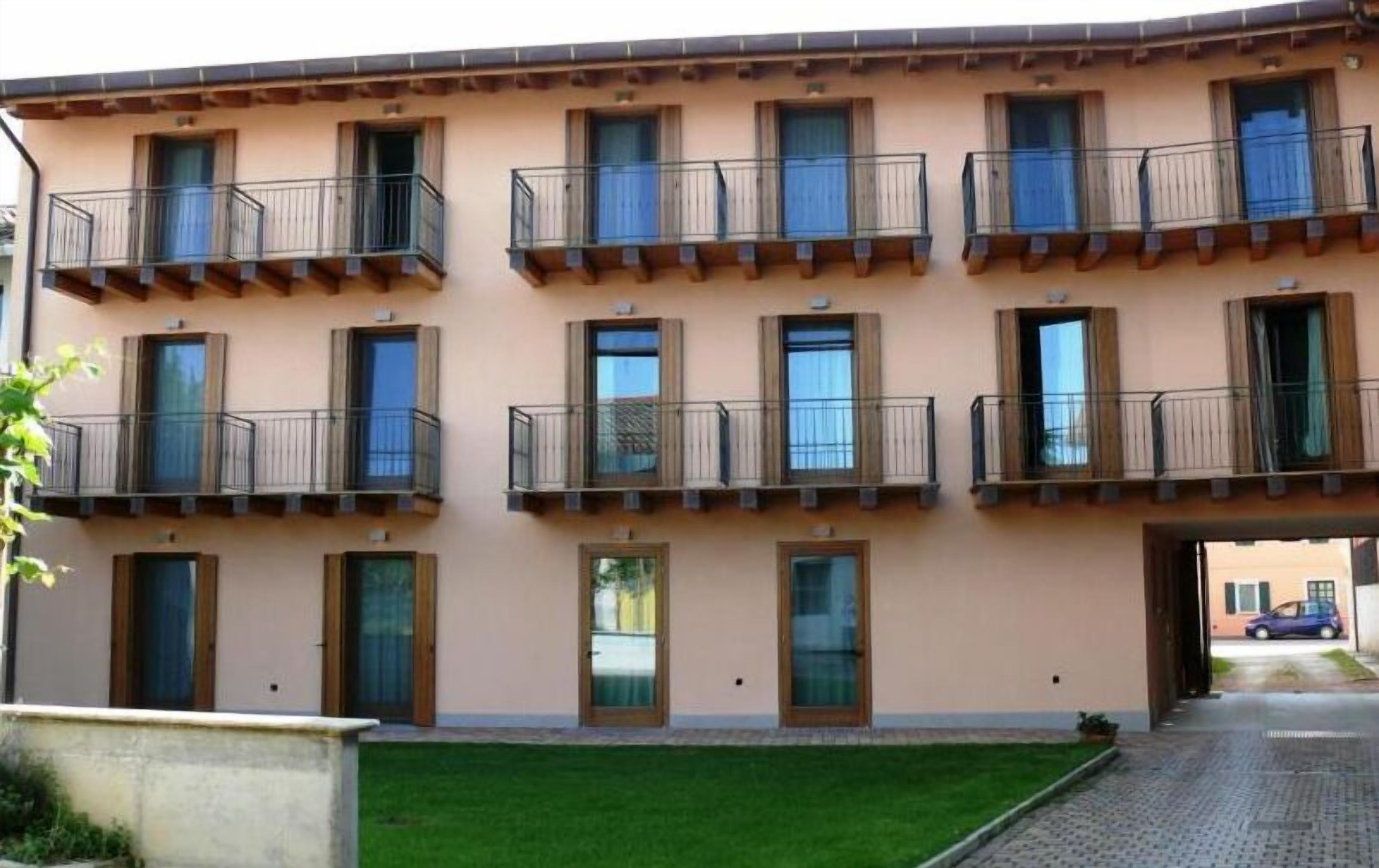 A multi-story building with balconies, a flat roof, and a paved entrance area.