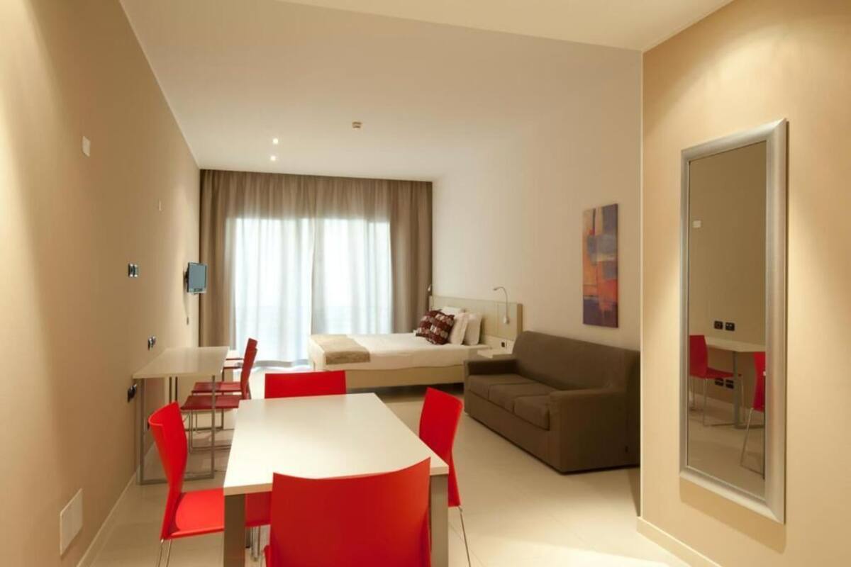 Quarto de hotel moderno com área de refeições, sofá, cama e um espelho grande.