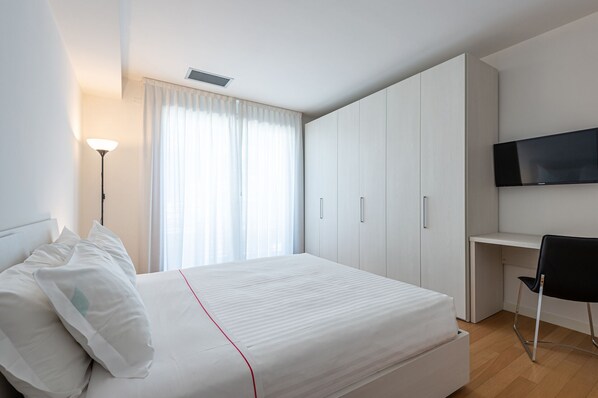 Un dormitorio con cama, escritorio, silla, televisor y armario.