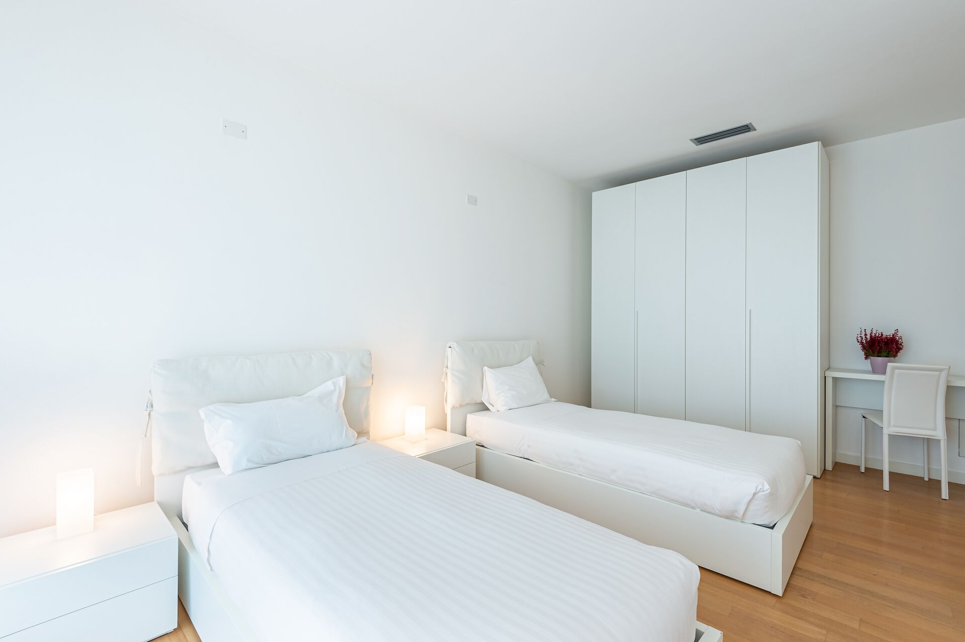 Une chambre à coucher au style minimaliste, avec deux lits, un bureau et une armoire.