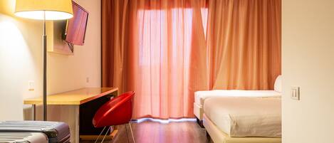 Habitación de hotel con cama, escritorio, silla, televisión y lámpara.