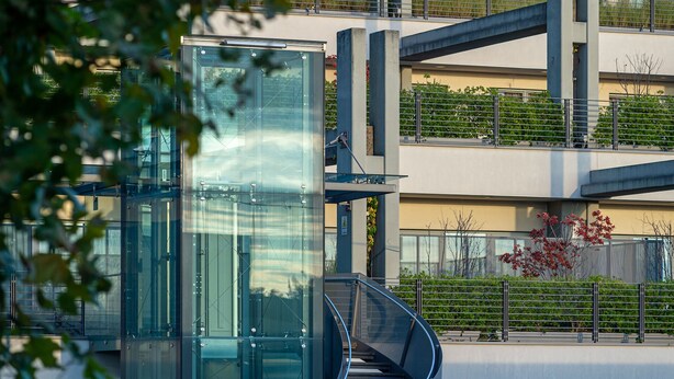 Un bâtiment moderne doté d’un ascenseur en verre, de plusieurs étages et d’un balcon agrémenté de plantes.