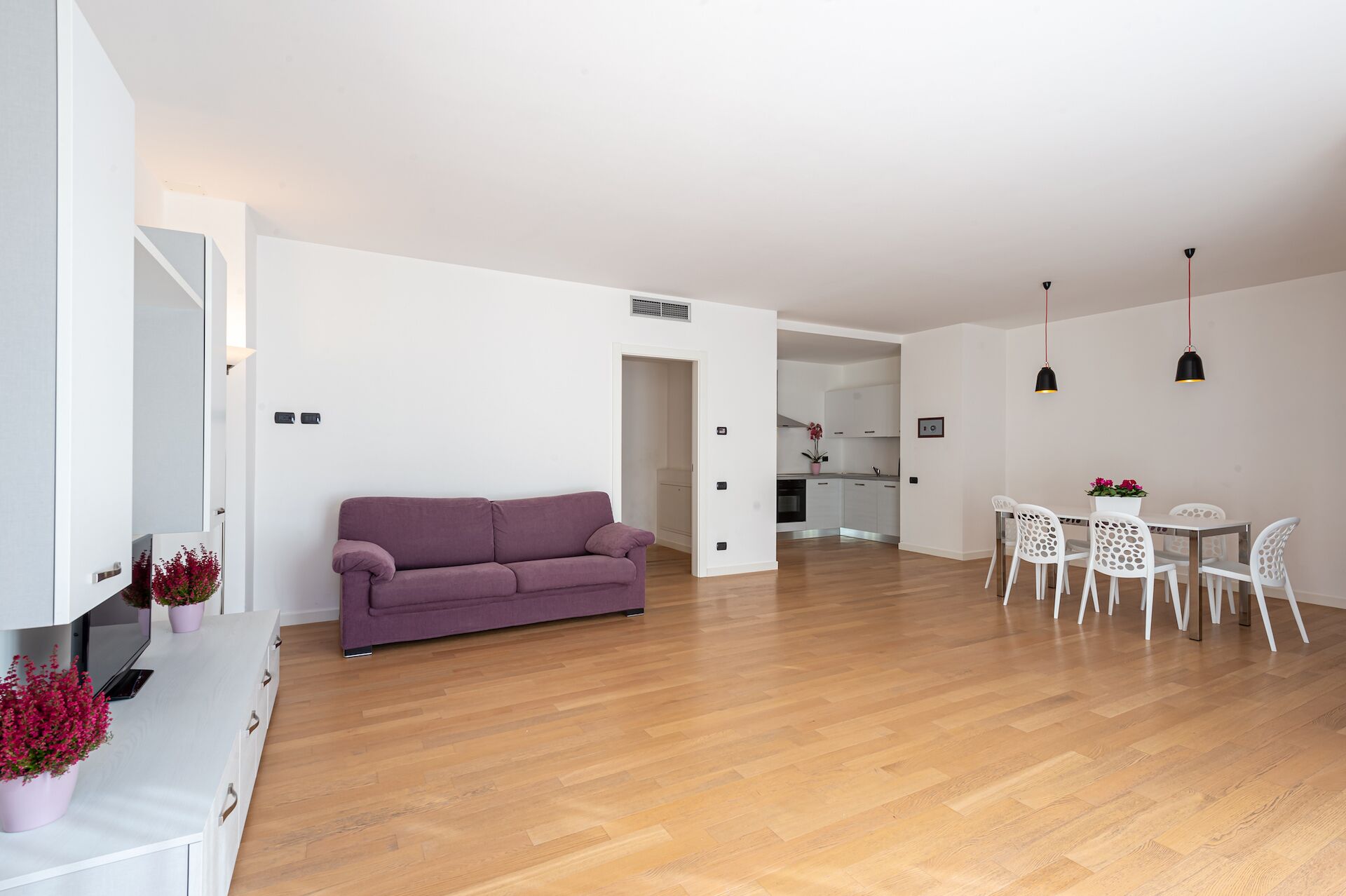 A modern living room with a sofa, dining table, chairs, and a kitchen area in the background.
