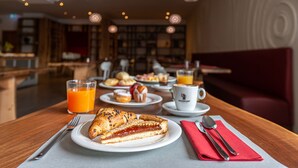 Une table dressée pour le petit-déjeuner, avec des croissants, des pâtisseries et du jus d’orange.