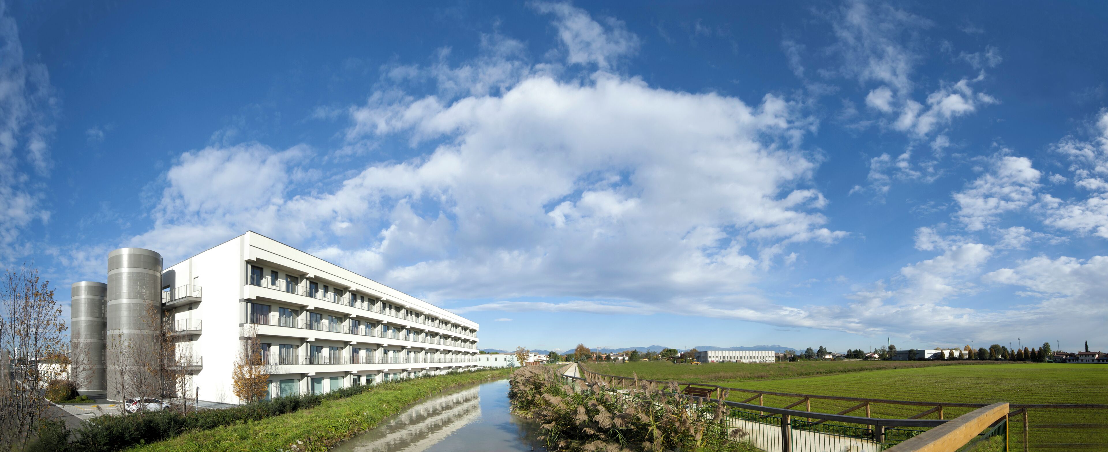 Un bâtiment moderne doté de nombreux balcons, avec une rivière en contrebas et un ciel bleu dégagé.