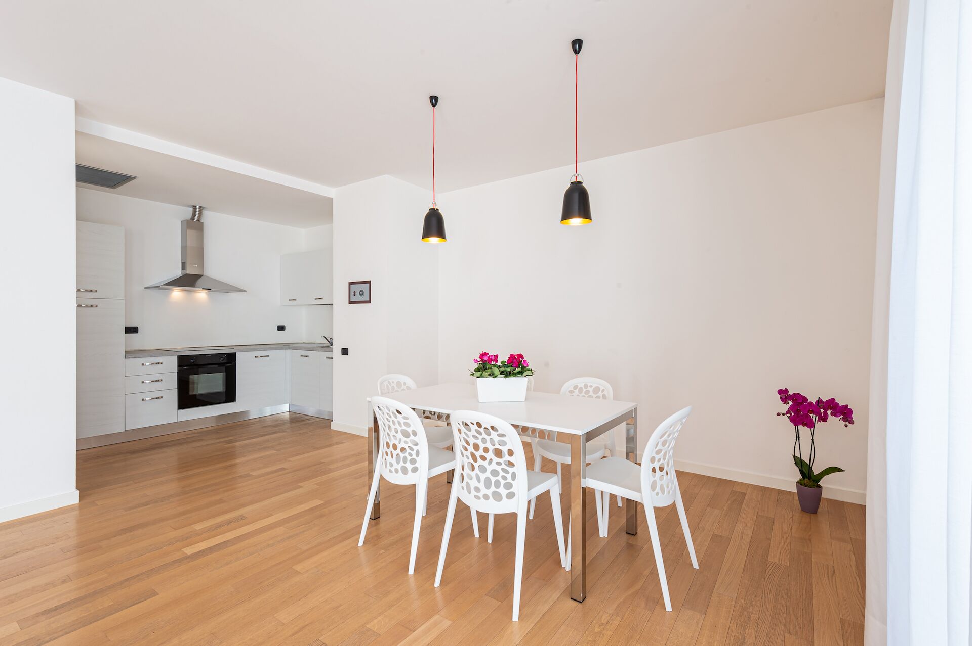 A modern kitchen with white cabinets, a stainless steel range hood, and a dining area with a white table and chairs.