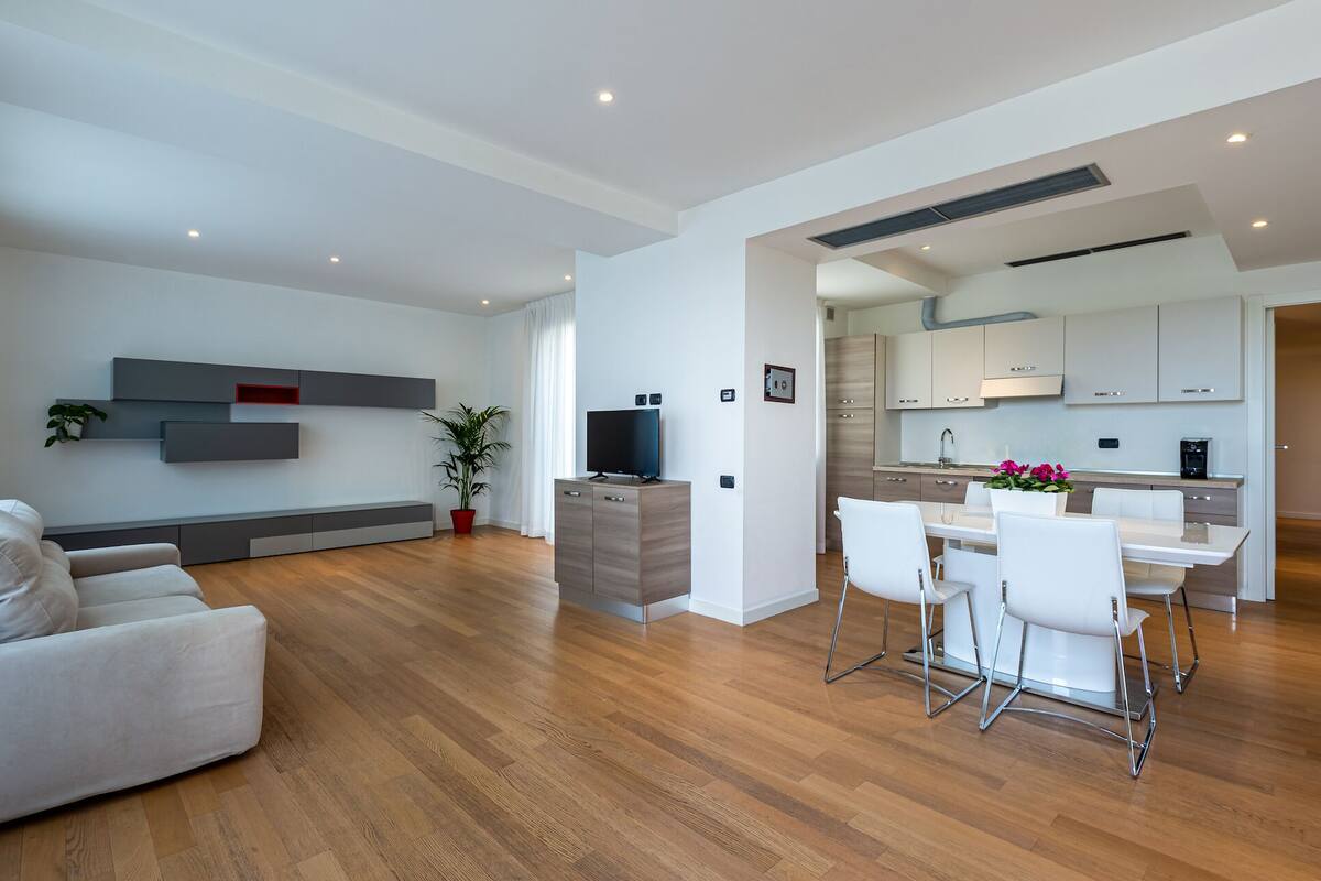 Uma sala de estar moderna com um sofá, uma TV e uma área de jantar com cadeiras e uma mesa.