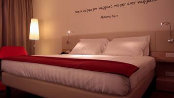 Habitación de hotel con cama, una silla roja, lámpara y una cita en la pared.
