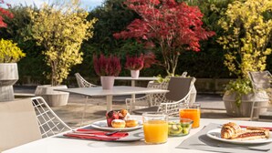 Un espace de restauration en plein air avec une table dressée pour le petit-déjeuner, comprenant des viennoiseries et un verre de jus d’orange.