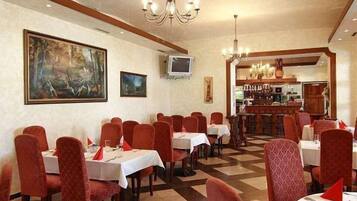 Um restaurante com cadeiras estofadas em vermelho, toalhas de mesa brancas e chão xadrez.