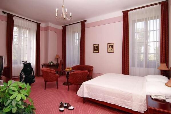 Habitación de hotel con cama, escritorio, silla, planta y perchero.