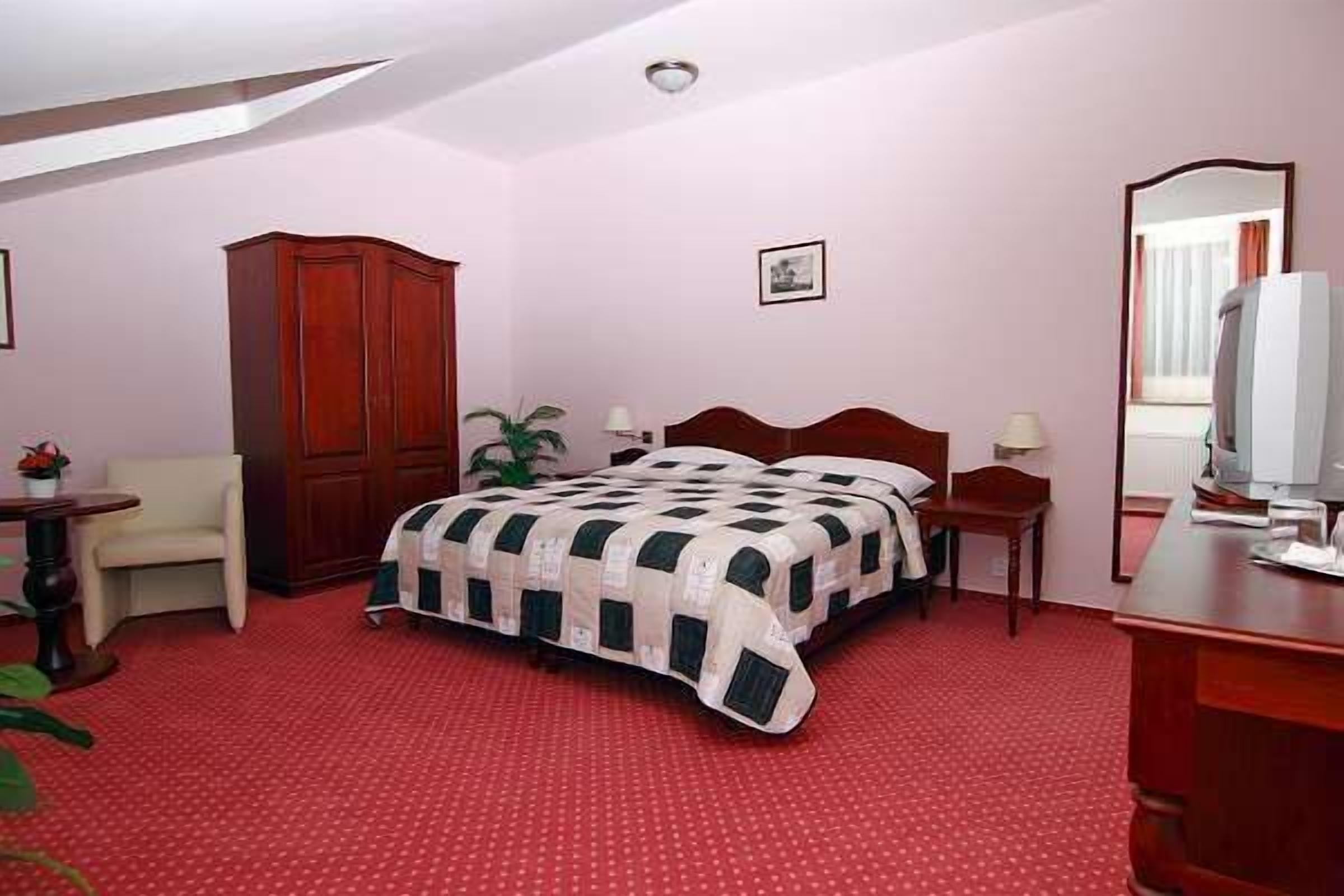 A bedroom with a bed, a wardrobe, a desk, a chair, and a mirror.