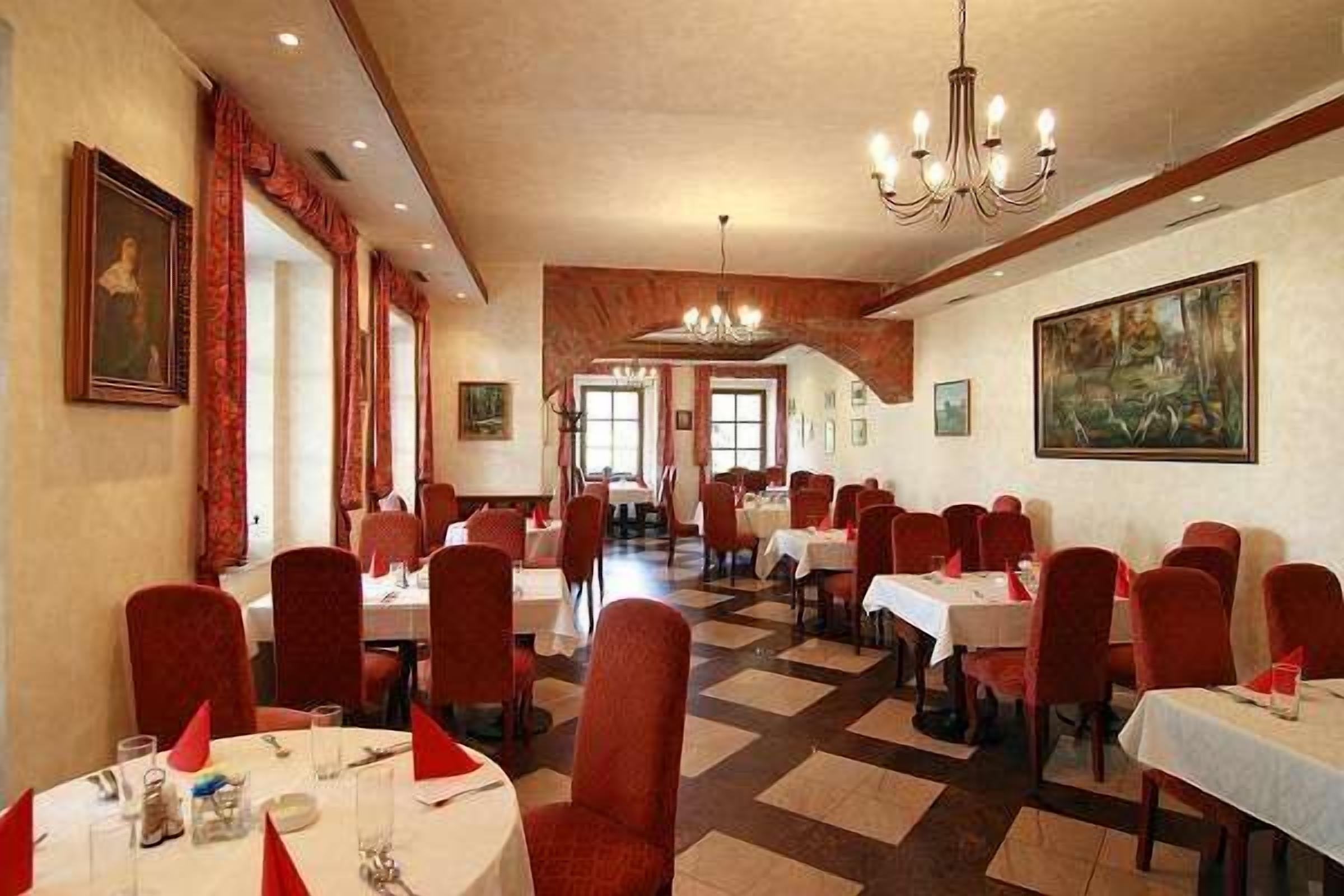 A dining area with multiple tables and chairs, a chandelier, and artwork on the walls.