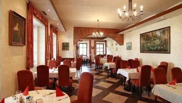 A dining area with multiple tables and chairs, a chandelier, and artwork on the walls.