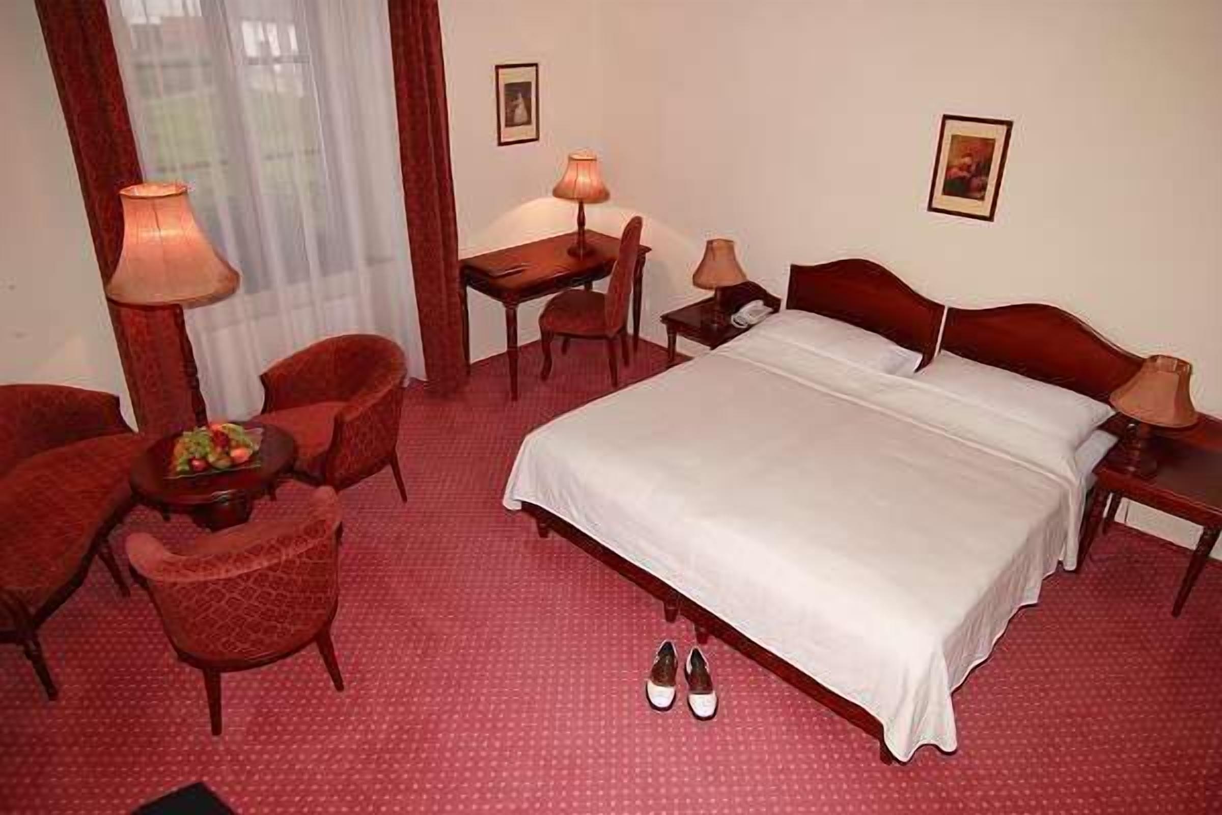 A hotel room with a bed, two chairs, a desk, and a lamp.