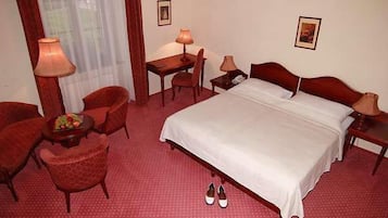A hotel room with a bed, two chairs, a desk, and a lamp.