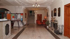 Un vestíbulo con suelo de mármol, un mostrador de recepción, una escalera y una zona de estar con chimenea.