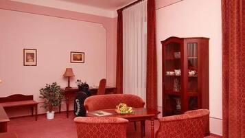 A room with a red carpet, a wooden cabinet, two chairs, a table, a lamp, and two framed pictures on the wall.
