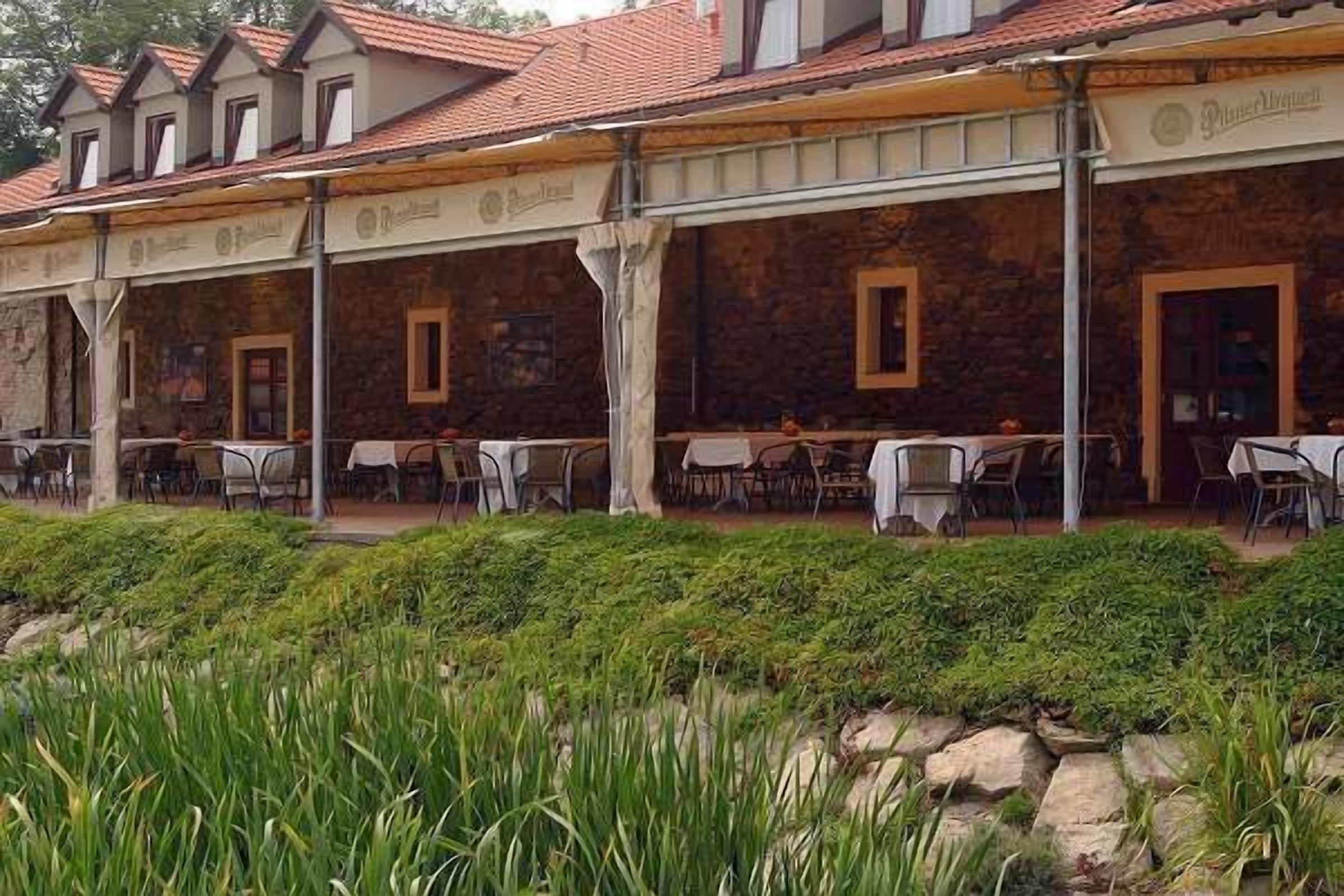 A stone building with a tiled roof, outdoor seating area with tables and chairs, and a well-maintained garden area with green plants.