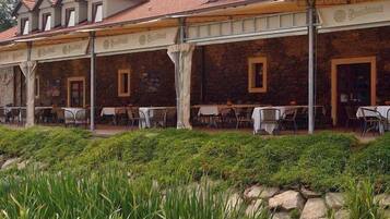 A stone building with a tiled roof, outdoor seating area with tables and chairs, and a well-maintained garden area with green plants.